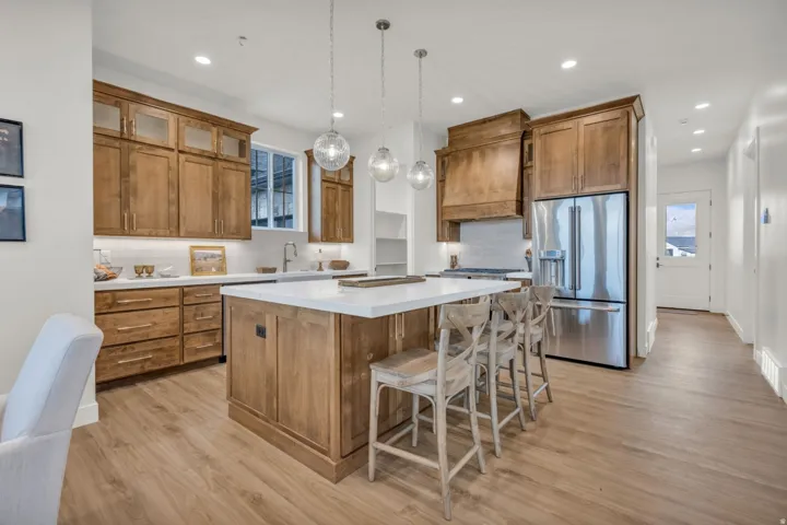 Kitchen featuring wood cabinetry, a center island with countertop seating, stainless steel refrigerator, white countertops, and wood-finish flooring