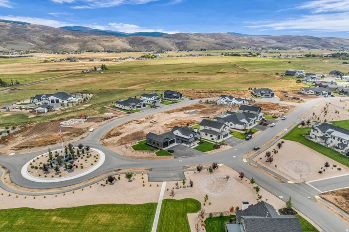 Community of modern homes with dark roofs, paved streets, and landscaped common areas, set against a backdrop of rolling hills and open fields