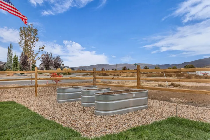 Manicured lawn area with gravel accents, featuring three raised metal planters and a post-and-rail fence