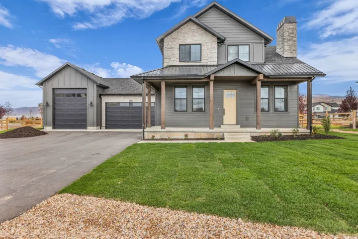 Two-story residence featuring a stone and siding exterior, metal roof accents, an inviting front porch with wood columns, and an attached two-car garage with board and batten siding