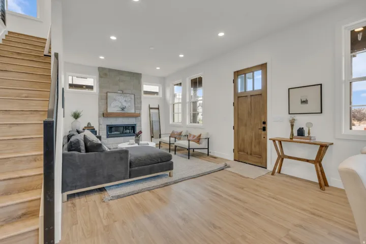 Recessed lighting illuminating wood-finish flooring, a stone-clad fireplace with a wood mantle, and a wood-paneled entry door