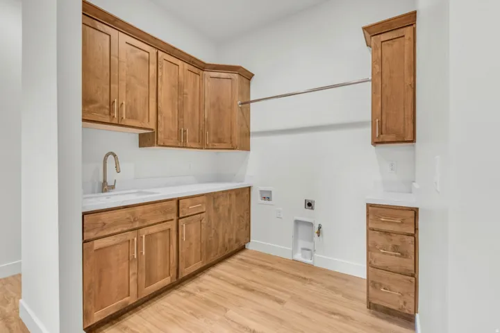 Wood-finish flooring with extensive wood cabinetry, white countertops, built-in sink, and a clothes hanging rod