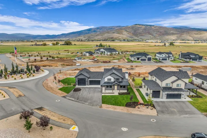 Newly constructed residential development featuring a modern farmhouse architectural style, dark asphalt shingle roofing, and a prominent mountain backdrop