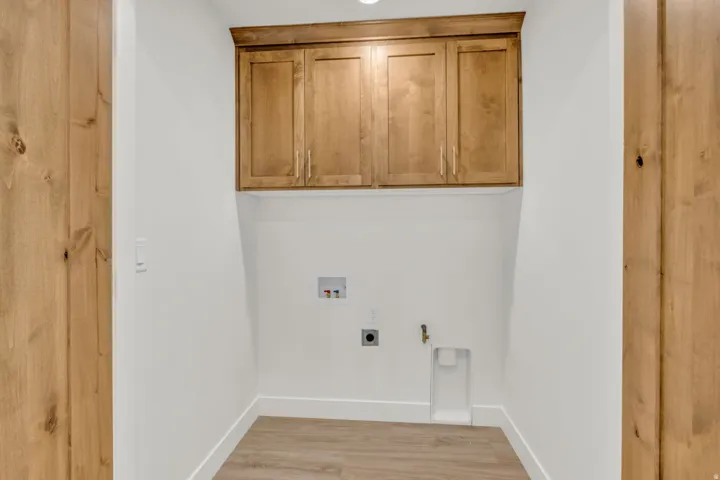 Laundry area with wood-finish cabinetry, light wood-finish flooring, and white walls