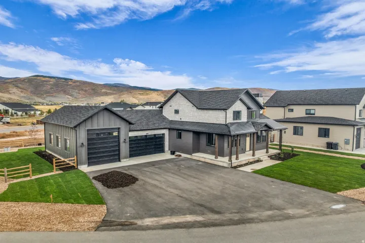 Modern farmhouse exterior with stone and vertical siding accents, a covered front porch, an attached three-car garage, and a separate detached garage structure