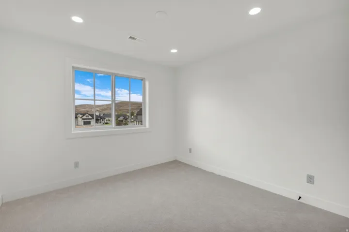 Neutral wall color, recessed ceiling lighting, light-toned carpeting, and a window with white trim