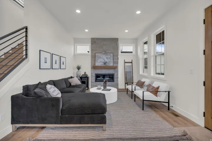 Recessed lighting, wood-finish flooring, stone-clad fireplace with wood mantel, multiple windows, and a staircase with metal railings