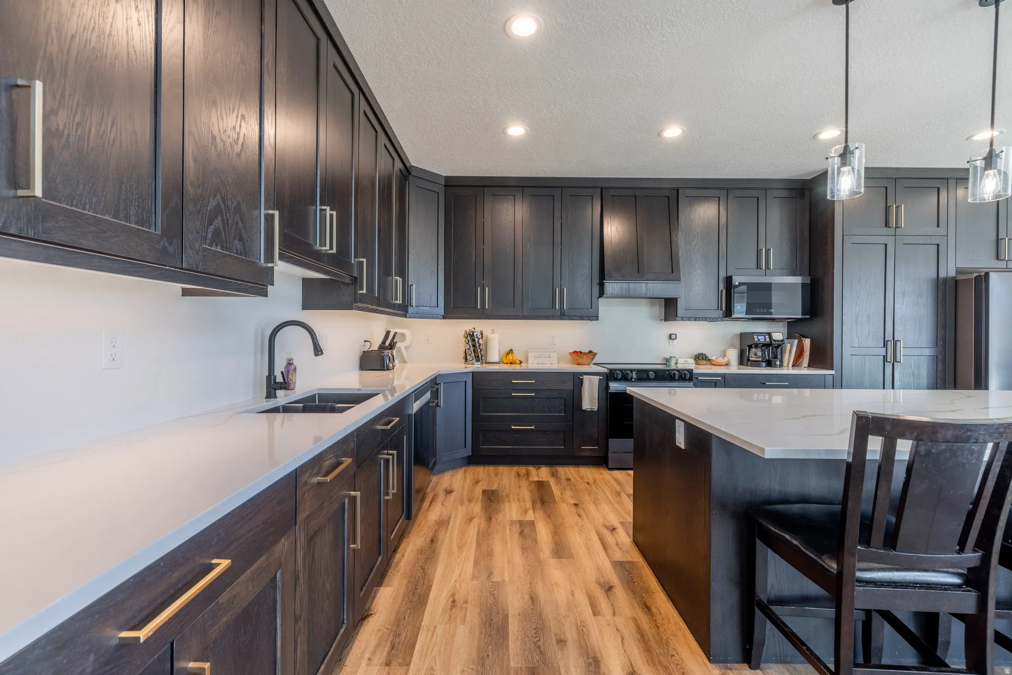 Kitchen featuring extensive dark-stained cabinetry, light-toned countertops, wood-finish flooring, recessed lighting, and a kitchen island with pendant lighting