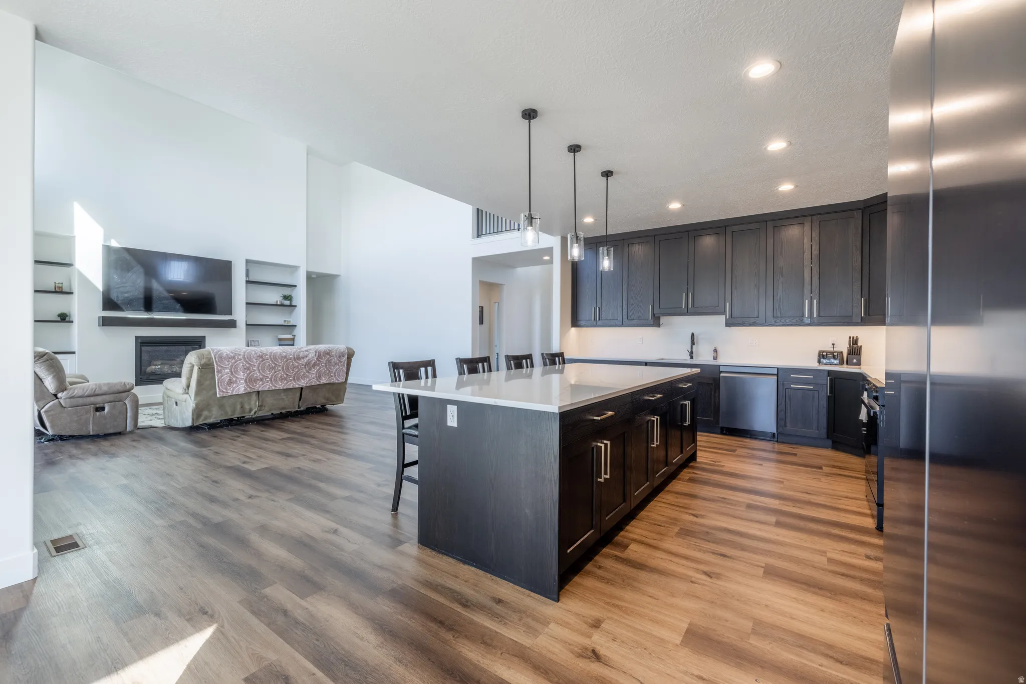Kitchen and living area featuring wood-finish flooring, a kitchen island with seating, dark cabinetry, and recessed lighting