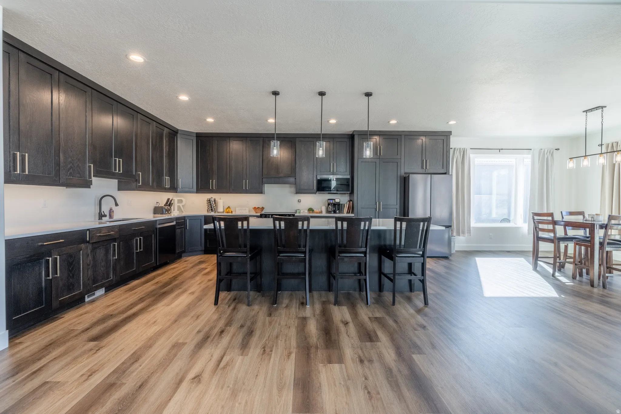 Spacious kitchen featuring dark wood-finish cabinetry, light countertops, wood-finish flooring, a large island with seating, and recessed lighting