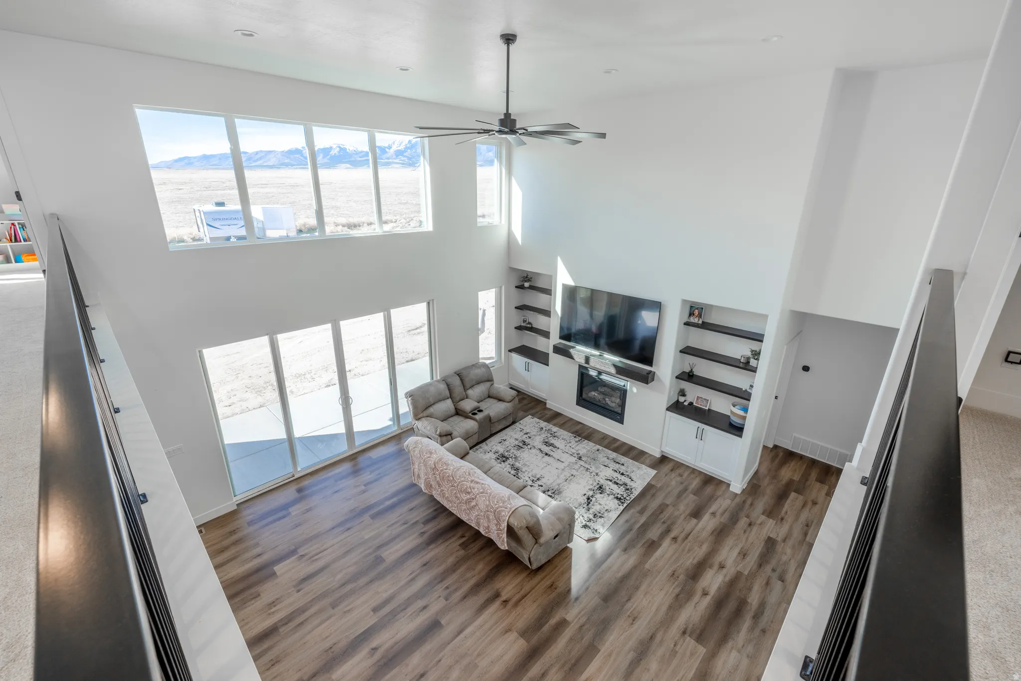Vaulted ceiling with a ceiling fan, wall of windows, sliding glass doors, wood-finish flooring, and built-in shelving with a fireplace