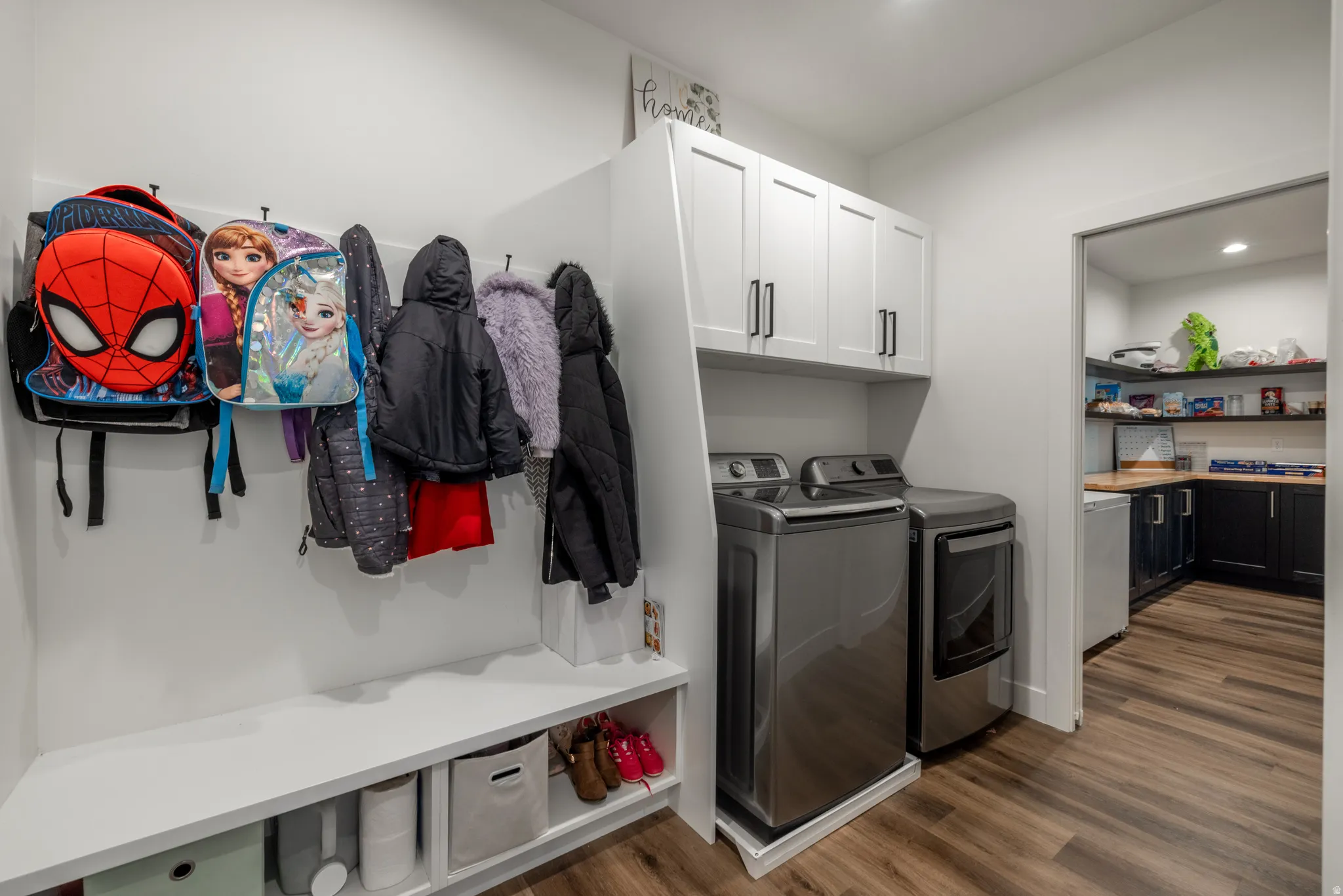 Built-in hall tree with storage bench, white upper cabinetry, and wood-finish flooring throughout
