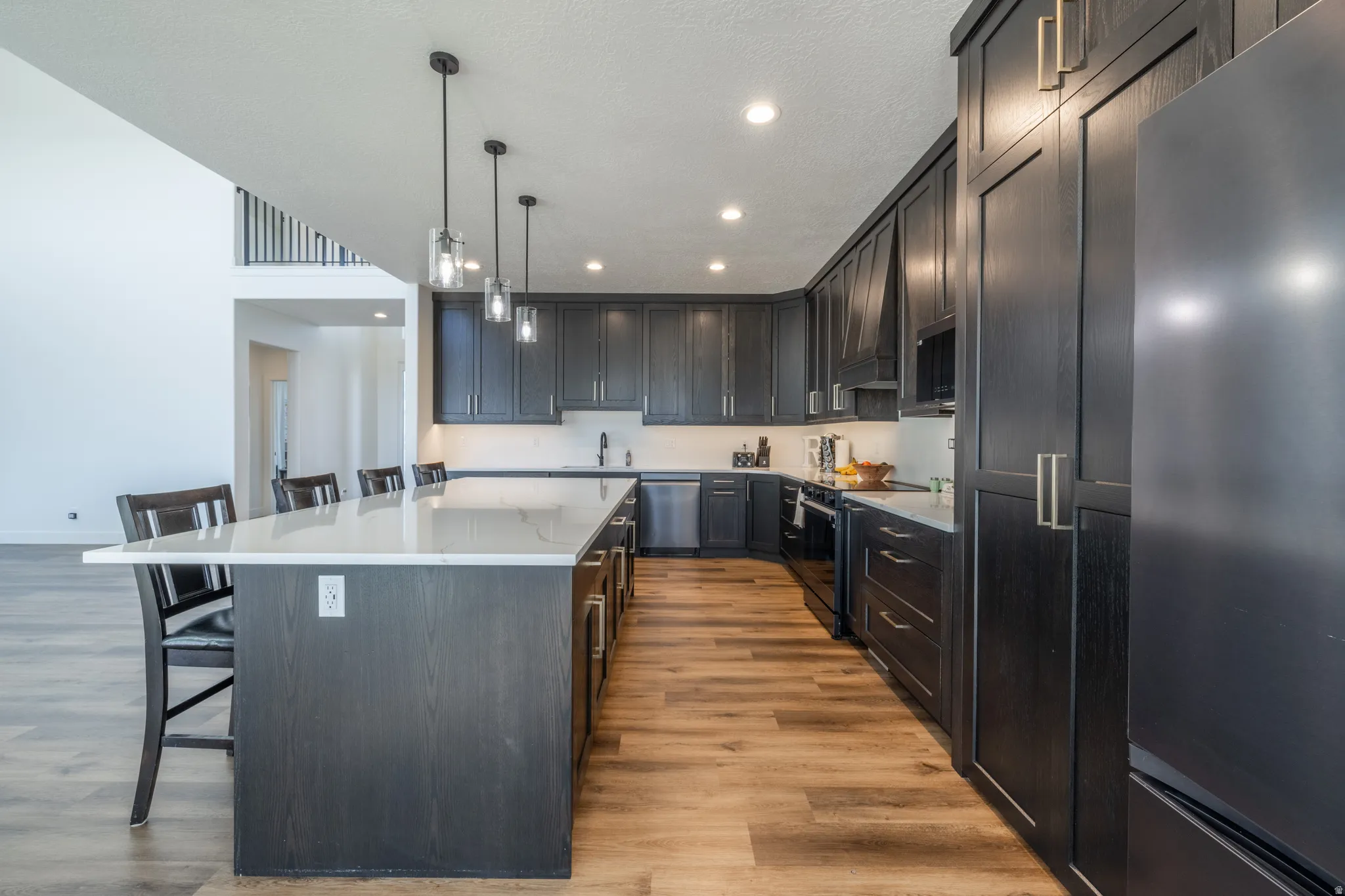 Kitchen featuring dark wood-finish cabinetry, light stone countertops, stainless steel appliances, a center island with seating, and wood-finish flooring