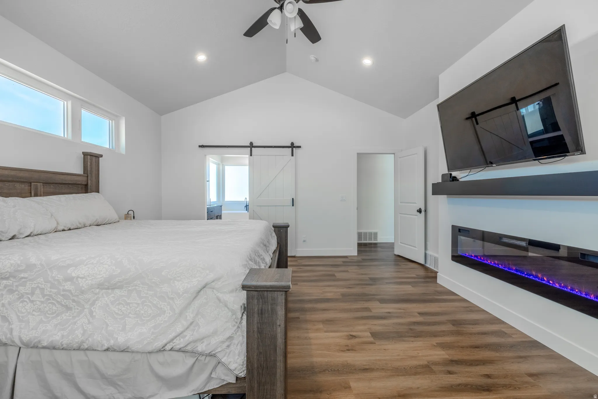 Primary Bedroom,, Vaulted ceiling with a ceiling fan, transom windows, wood-finish flooring, and an electric fireplace with a floating mantel