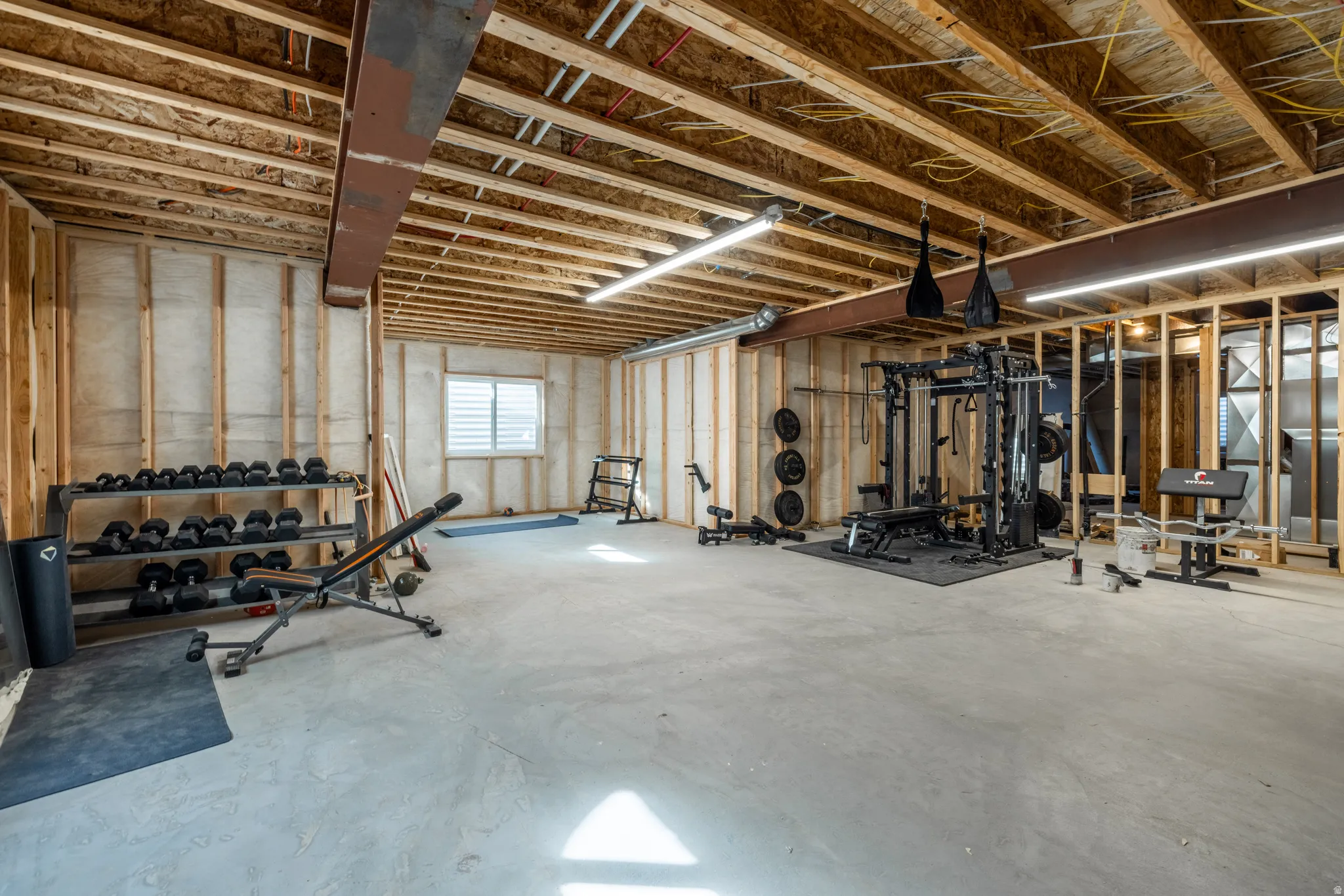 Unfinished basement featuring exposed wood joists, concrete flooring, and a single window with blinds