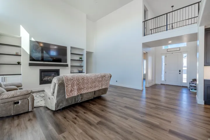 Open-concept living space with wood-finish flooring, a contemporary fireplace, built-in shelving, and a two-story entry with an upper-level railing