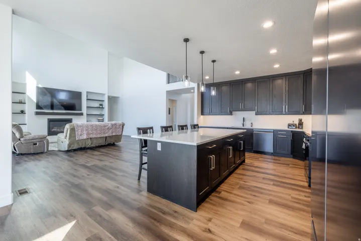 Kitchen and living area featuring wood-finish flooring, a kitchen island with seating, dark cabinetry, and recessed lighting