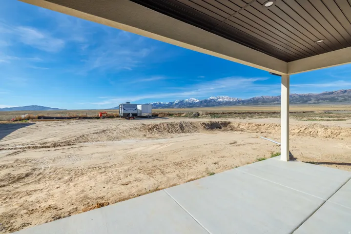 Expansive concrete patio with a covered outdoor area, featuring a slatted ceiling and recessed lighting, overlooking a vast desert landscape with distant snow-capped mountains