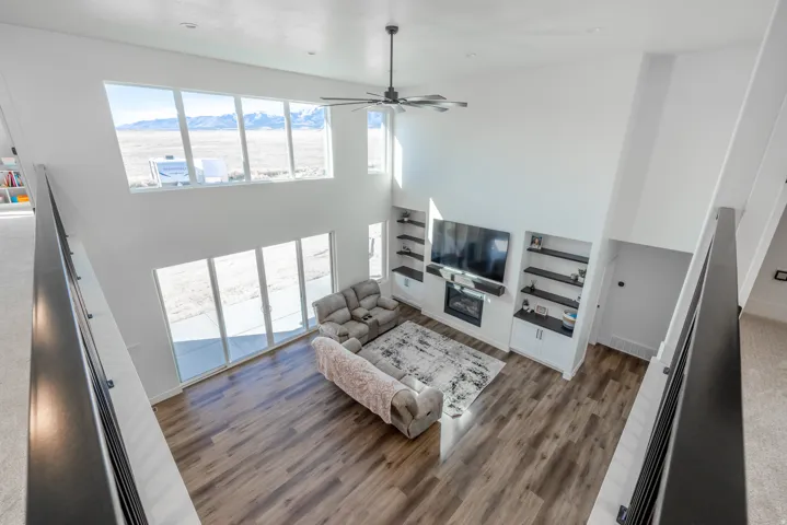 Vaulted ceiling with a ceiling fan, wall of windows, sliding glass doors, wood-finish flooring, and built-in shelving with a fireplace