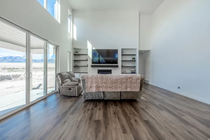 Spacious living area featuring high ceilings, wood-finish flooring, a built-in media center with shelving, a fireplace, and large sliding glass doors providing access to an outdoor patio