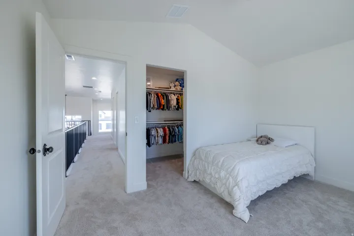Bedroom 4~ Carpeted room featuring a vaulted ceiling and an open closet with built-in shelving and hanging rods