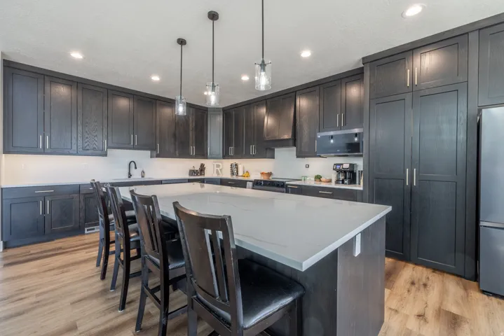 Expansive kitchen island with a light-toned countertop, dark wood-finish cabinetry, wood-finish flooring, and pendant lighting