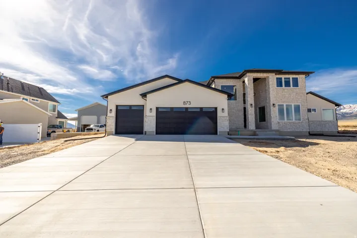 Contemporary exterior with stone and stucco finishes, a two-car garage with black doors, a concrete driveway, and a visible mountain backdrop