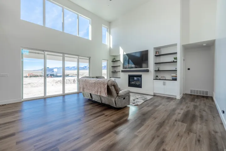 Vaulted ceiling with high windows, wood-finish flooring, built-in shelving, integrated fireplace, and large sliding glass doors