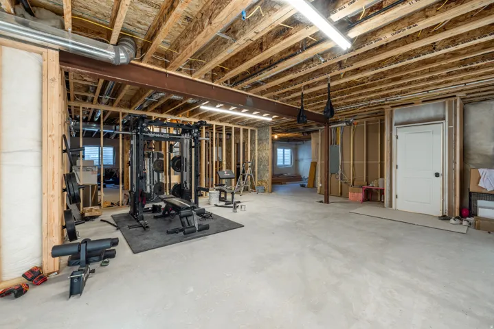Unfinished basement with concrete flooring, exposed wood ceiling joists, and visible structural framing