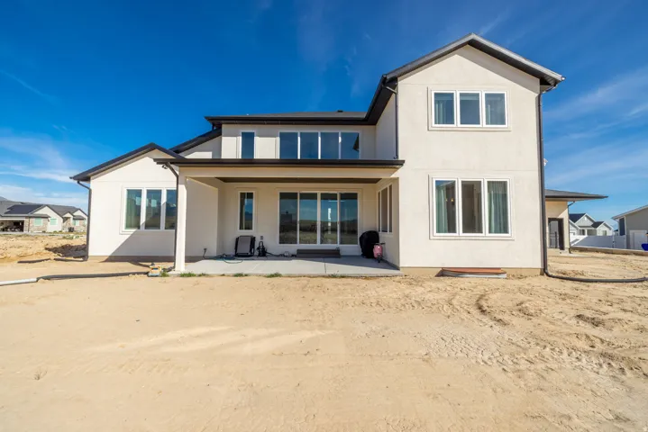 Rear exterior featuring a covered patio, multiple large windows, and a sand-finish stucco facade