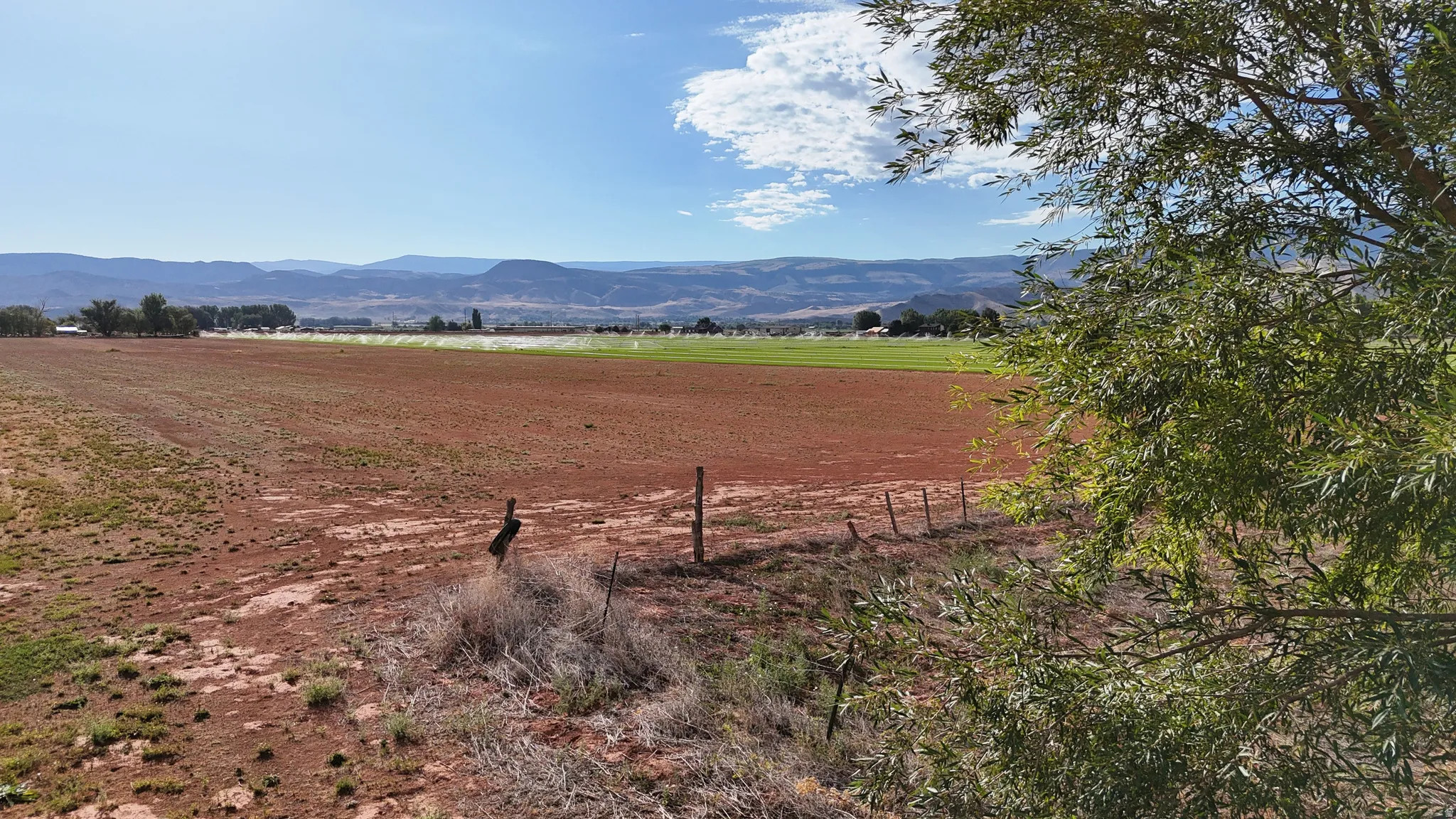 Expansive open land with distant mountain backdrop, partially fenced boundary, and scattered vegetation
