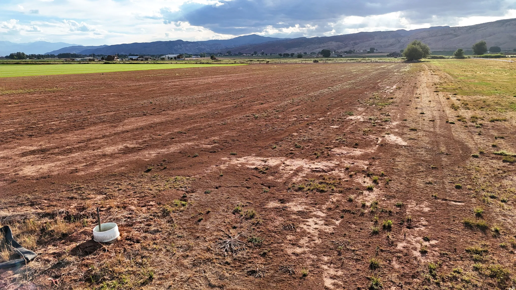 Expansive agricultural land featuring a tilled field, a green cultivated area, and distant mountains