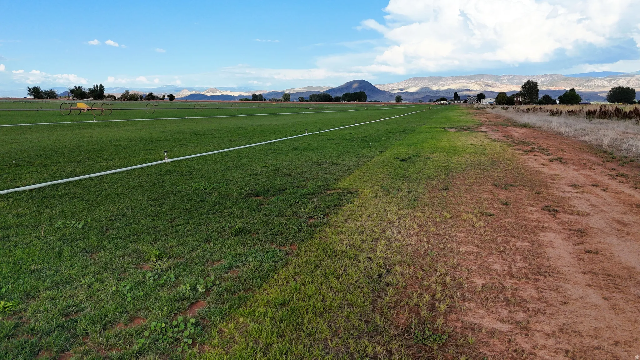 Expansive green field with irrigation lines, bordered by a natural dirt path