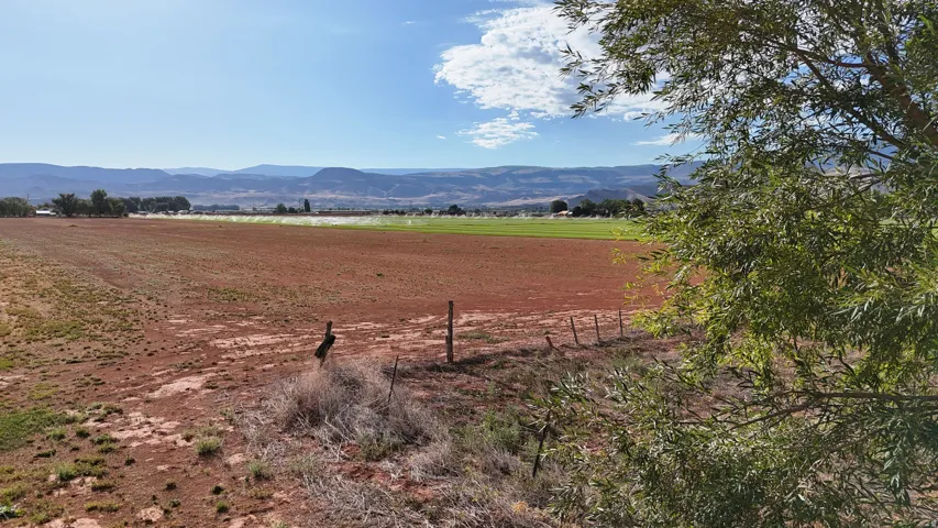Expansive open land with distant mountain backdrop, partially fenced boundary, and scattered vegetation