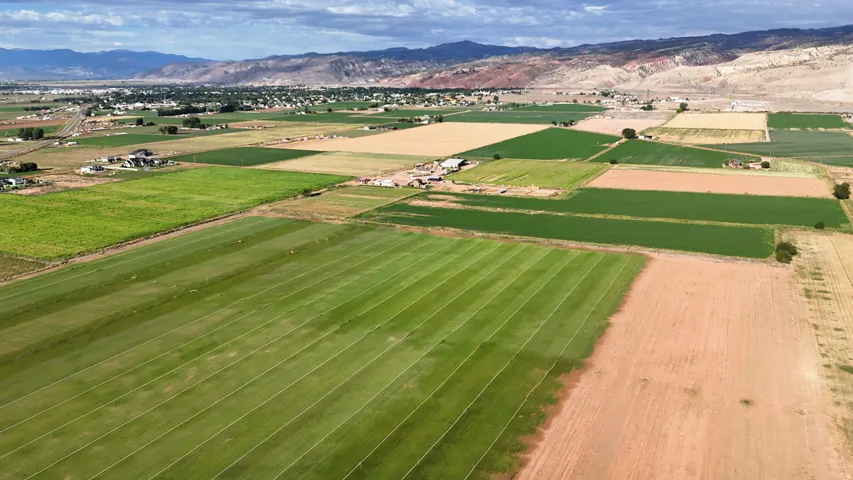 Expansive agricultural land featuring varied crop fields, distant residential areas, and mountainous terrain