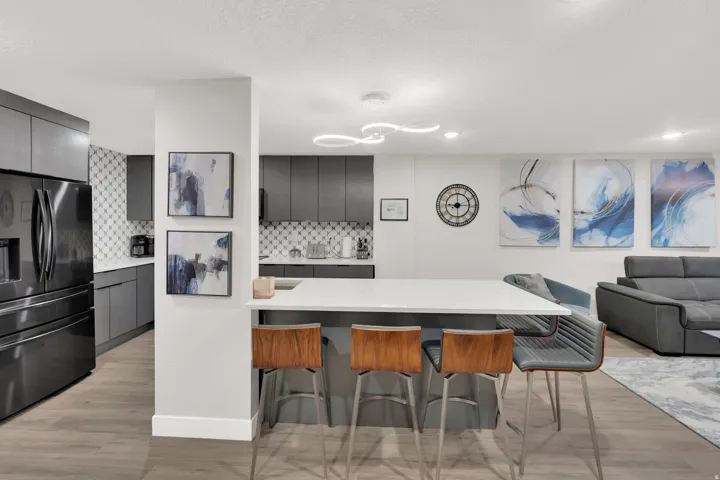 Modern kitchen featuring a large island, dark gray cabinetry, stainless steel refrigerator, and patterned tile backsplash