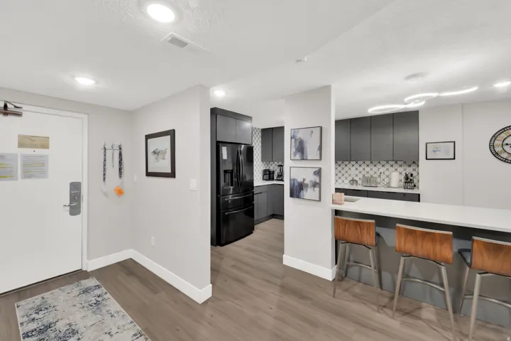 Wood-finish flooring, recessed lighting, and a kitchen featuring dark cabinetry, a patterned backsplash, and an extended countertop island