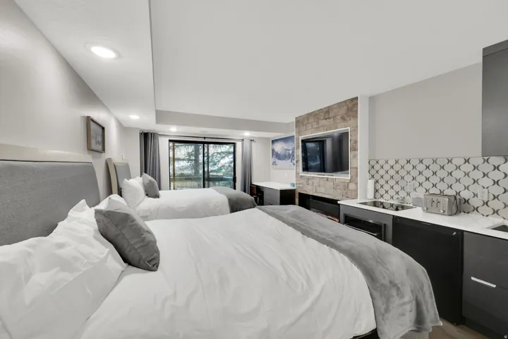 Recessed lighting, wood-finish flooring, full-height sliding glass doors, stone-look accent wall, and built-in kitchenette with a decorative tile backsplash