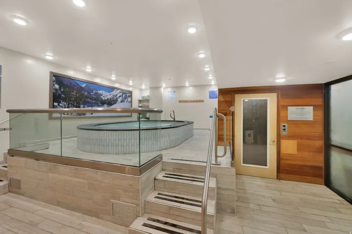 Built-in hot tub with surrounding glass railing, light-toned tile flooring, wood paneling, and recessed lighting