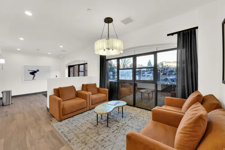 Spacious room featuring wood-finish flooring, a contemporary chandelier, recessed lighting, and large windows with dark drapery