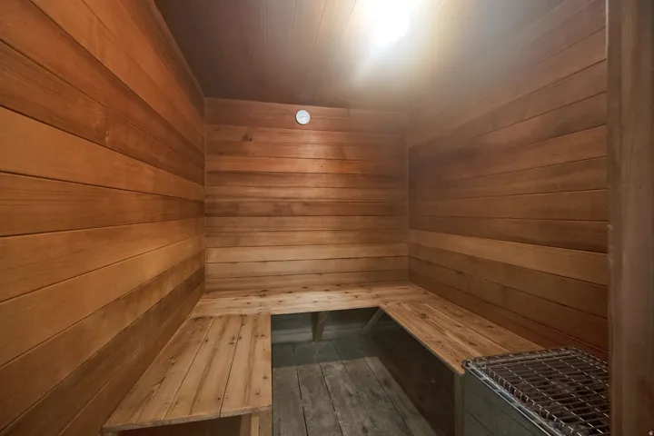 Wood-paneled sauna featuring built-in benches, a temperature gauge, and a heat source with protective grating