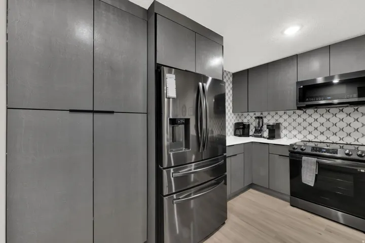 Stainless steel refrigerator, built-in microwave, dark gray cabinetry, white countertops, and patterned tile backsplash