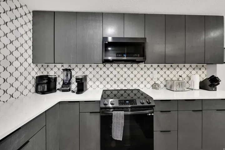 Kitchen featuring dark flat-panel cabinetry, white countertops, a patterned backsplash, and a built-in microwave