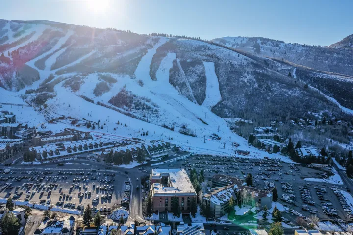 Snow-covered mountain terrain with visible ski runs, surrounding residential structures, and extensive parking areas