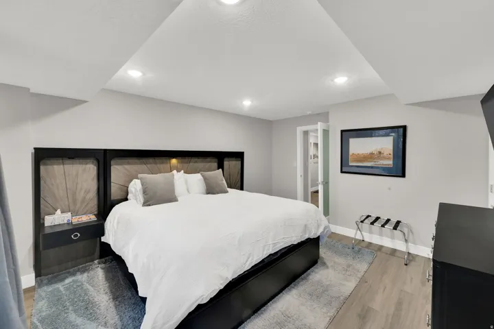 Recessed lighting, wood-finish flooring, light gray wall color, and a built-in headboard with integrated lighting