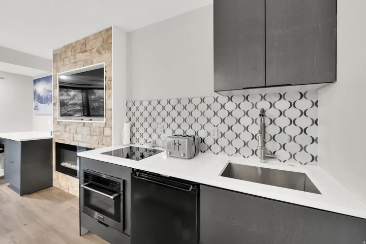 Compact kitchen featuring white countertops, an undermount sink, geometric tile backsplash, and dark cabinetry