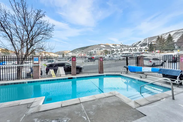 Outdoor swimming pool with concrete decking, surrounded by a black metal fence with brick pillars, set against a mountain backdrop