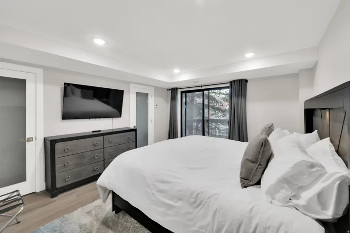 Recessed ceiling lighting, wood-finish flooring, sliding glass door with exterior access, frosted glass doors, and a built-in wall-mounted television