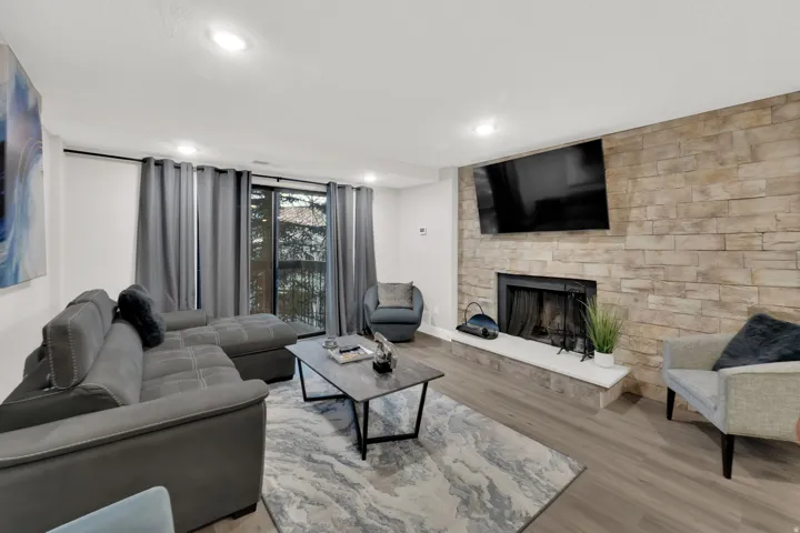 Living area featuring a stone accent wall, fireplace with hearth, recessed lighting, and wood-finish flooring