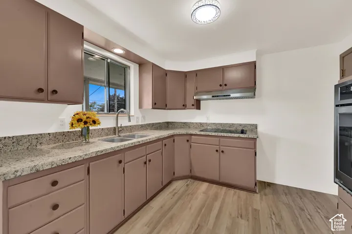 Kitchen featuring New LVP wood-finish flooring, L-shaped countertops, stainless steel appliances, a double basin sink, and ample cabinetry